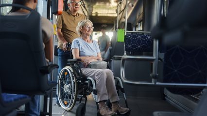 Happy disabled senior woman in a wheelchair and her husband traveling by a bus.