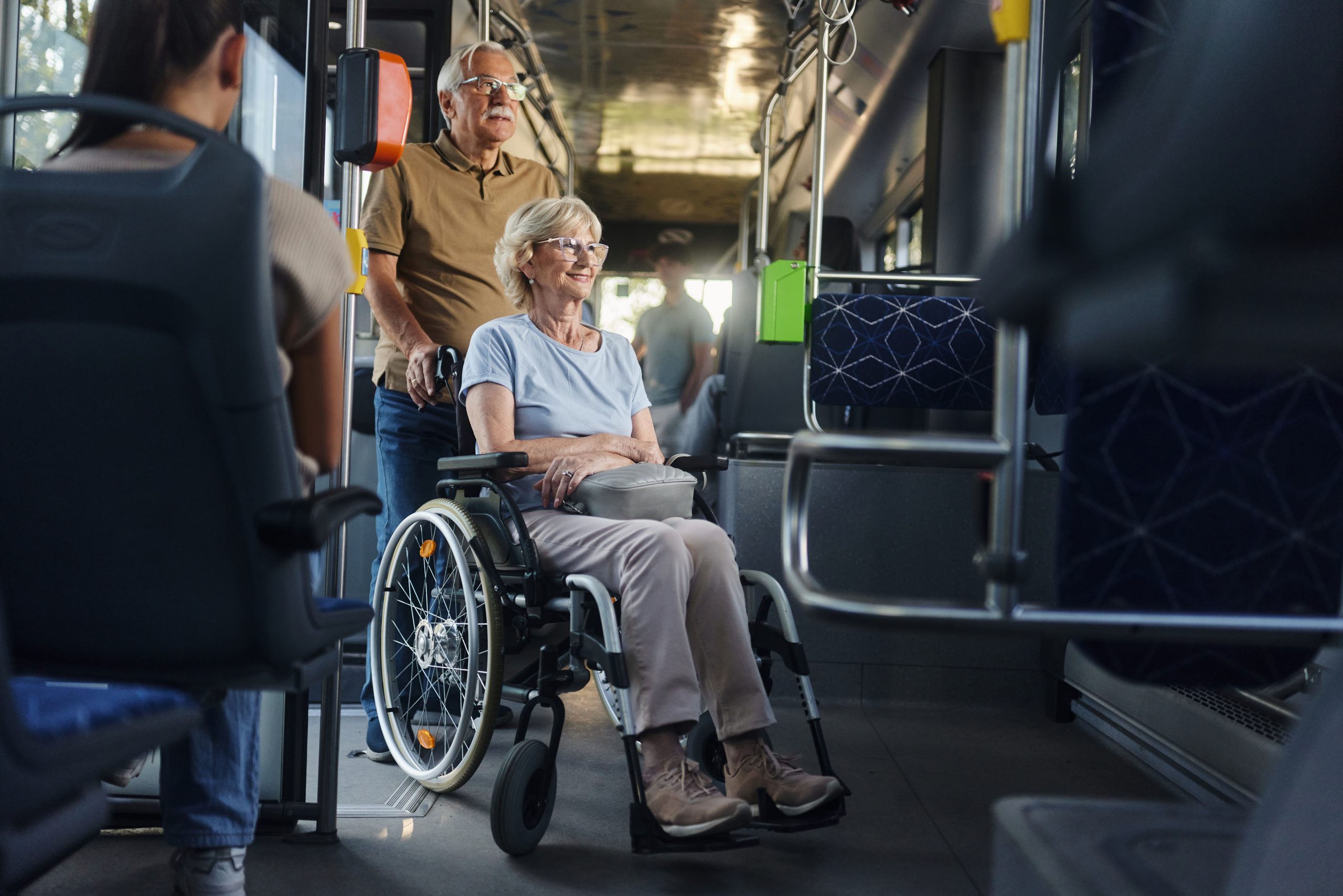 Happy disabled senior woman in a wheelchair and her husband traveling by a bus.